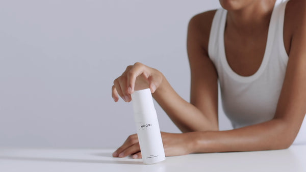 Woman in a white tank top holding NUORI Vital Foaming Cleanser.